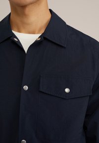 Marineblauwe, lichtgewicht shirt met een grote kraag, drukknoopsluiting en een borstzak met een zilverkleurige knoopdetails. Soepele textuur.
