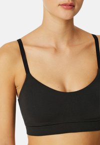 Sort bralette med tynde stropper, lavet af blødt, strækbart stof. Den har en rund halsudskæring og et bredt bånd i bunden.