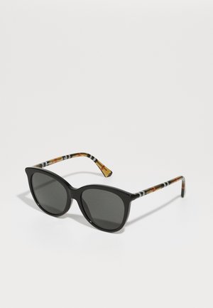Gafas de sol de marco negro con lentes grises. Las varillas presentan un diseño colorido y con patrones en naranja, negro y blanco. Forma elegante y de gran tamaño.