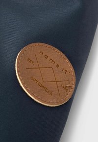 Jūras zila auduma ar teksturētu virsmu; iekļaujapa apaļu brūnu ādas plāksni ar izspiestu dizainu un tekstu, tostarp "nosauc to" un "ĀRPREČI".