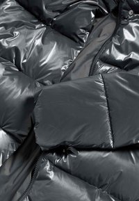 Puffet jakke i mørkegrå, lavet af skinnende materiale. Har quiltede sektioner, lynlås lukning og en glat tekstur.