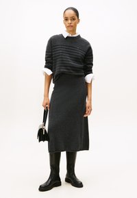 Donkergrijze sweater met horizontale strepen, gecombineerd met een bijpassende lange rok. Zwarte kniehoge laarzen en een kleine handtas maken de look compleet.