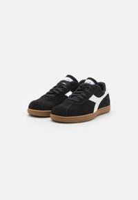 Svarte semskede sneakers med hvite detaljer, rund tå, snøring, og såle av gummi. Har polstret krage og tunge.