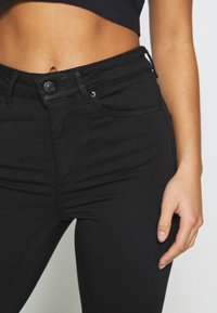 Pantalones vaqueros negros de talle alto y corte ajustado. Con cierre de botón y cremallera, cinco bolsillos y una textura suave y lisa.