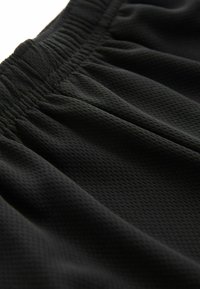 Pantaloni sportivi neri realizzati in tessuto a rete testurizzato, con vita elasticizzata e dettagli plissettati per una maggiore flessibilità.