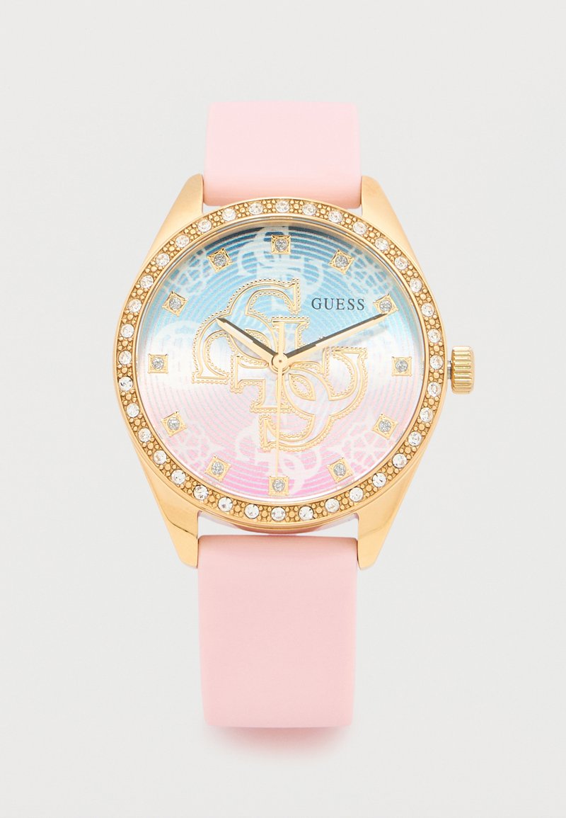 Ρολόι χειρός Guess σε χρυσό τόνο με ροζ λουράκι σιλικόνης, στεφάνη διακοσμημένη με κρυστάλλους και ιριδίζον καντράν με διακοσμητικά λογότυπα και δείκτες ώρας από κρύσταλλα.