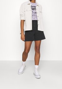 Vaaleabeige puuvillahousutakki, violetti graafinen t-paita, mustat farkkushortsit, valkoiset korkeavartiset tennarit ja valkoiset nilkkasukat.