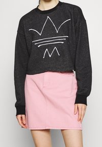 Svart kort sweatshirt med vit grafisk design, kombinerad med en ljusrosa denimkjol med framfickor och sömdekorationer.