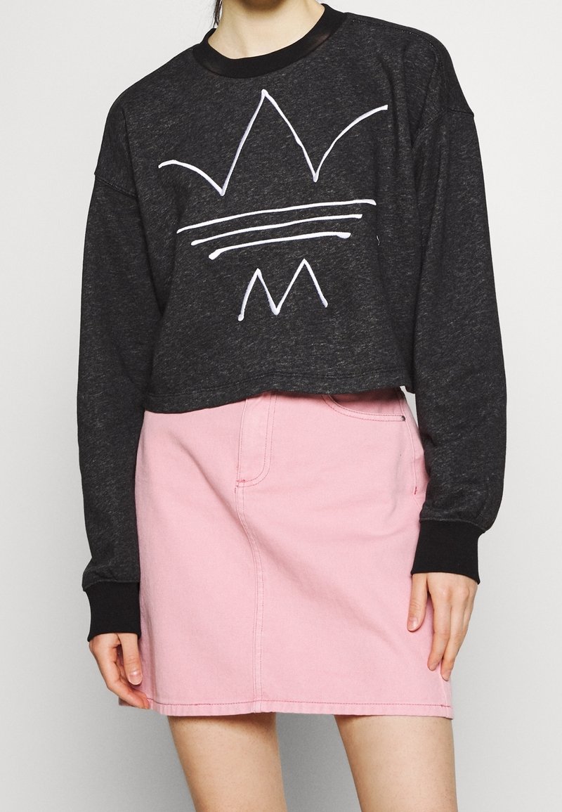 Svart kort sweatshirt med vit grafisk design, kombinerad med en ljusrosa denimkjol med framfickor och sömdekorationer.