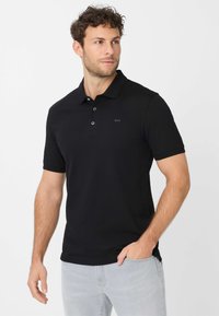 Zwarte polo shirt van zacht materiaal, met een klassieke kraag, drie knopen bij de hals en subtiele branding aan de voorkant.