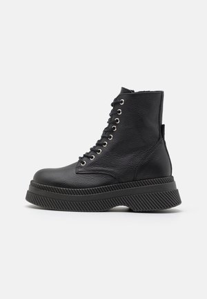 Black leather ankle boots with a textured finish, featuring metal eyelets, a thick rubber sole, and distinct ribbed accents.