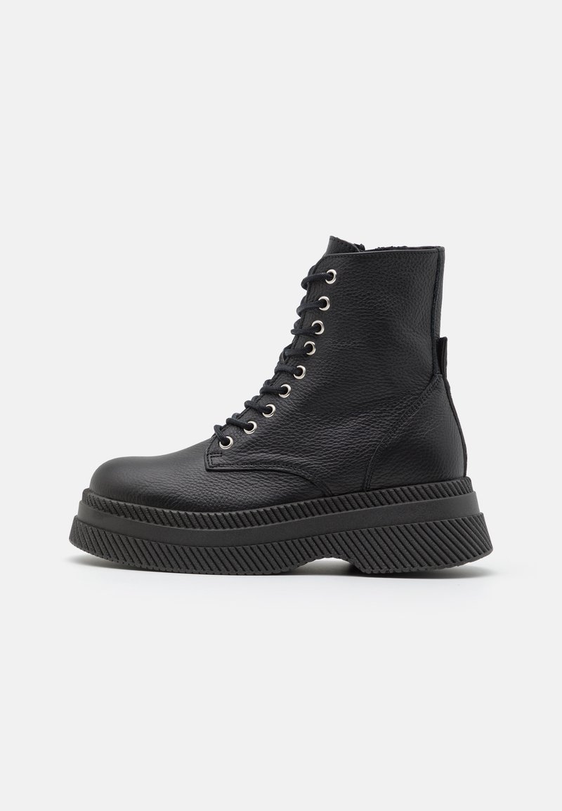 Botas de tobillo de cuero negro con un acabado texturizado, que presentan ojales metálicos, una suela de goma gruesa y acentos ribeteados distintos.
