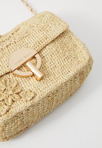 Geantă din paie cu un finisaj natural texturat, formă rectangulară, închidere circulară aurie și accente florale în față.