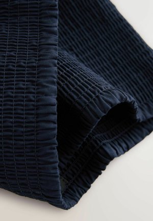 Granatowa, teksturowana tkanina z marszczeniami, ukazująca podwinięty brzeg i widoczne wypukłości na powierzchni. Miękki materiał, elastyczny kształt.