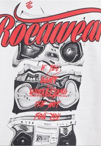 Roca Wear T-shirt featuring a graphic print of stacked boomboxes in black and grey, with bold red text overlay. White cotton material.