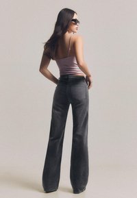 Pantaloni largi de culoare gri închis, confecționați dintr-un material moale asemănător cu pielea întoarsă. Au talie înaltă și buzunare în spate, asortați cu un top lilac mulat.