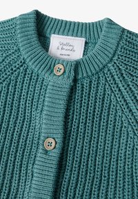 Strickjacke in Teal mit texturiertem Muster, rundem Halsausschnitt und zwei Knopfverschlüssen. Mit einem Etikett, das die Größe 62/68 angibt.