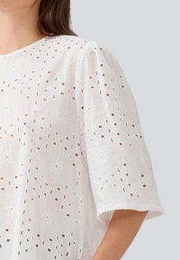 Blouse en coton blanc avec des fleurs brodées et des motifs découpés, présentant des manches courtes et bouffantes ainsi qu'un col rond.