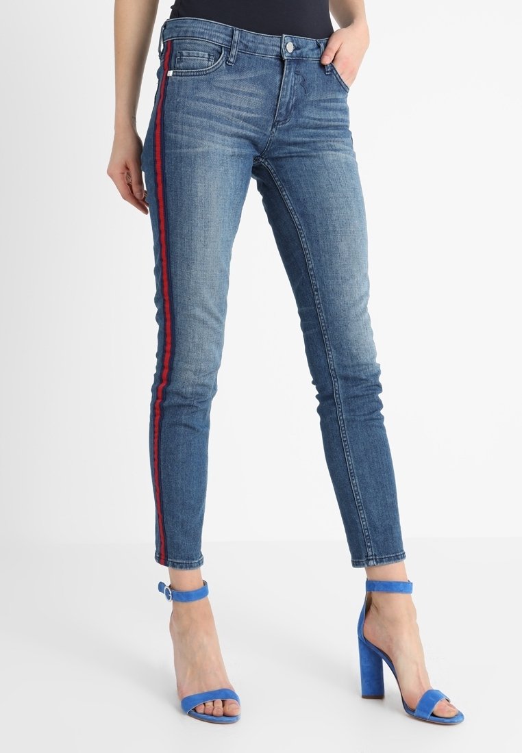 Jeans ajustados de mezclilla azul con franjas rojas en los laterales, cinco bolsillos y una cintura de altura media. El material tiene un ligero estiramiento para mayor comodidad.