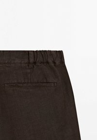Pantalons marron foncé à taille élastique en tissu texturé, comportant une poche arrière unique et un devant plat avec passants de ceinture.