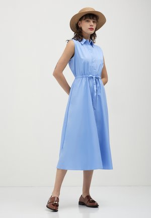 Abito senza maniche di colore azzurro chiaro con chiusura a bottoni, vita strizzata e gonna fluente, indossato con mocassini marroni e un cappello di paglia.