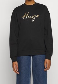 Zwarte sweatshirt van katoen, met een glanzend gouden "Hugo"-logo. Het heeft een ronde hals en een ontspannen pasvorm, met geribde boorden en zoom.