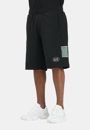 Pantaloncini neri al ginocchio con vita elastica, dettaglio tasca laterale grigio chiaro, logo EA7 vicino all'orlo, indossati con scarpe da ginnastica bianche.