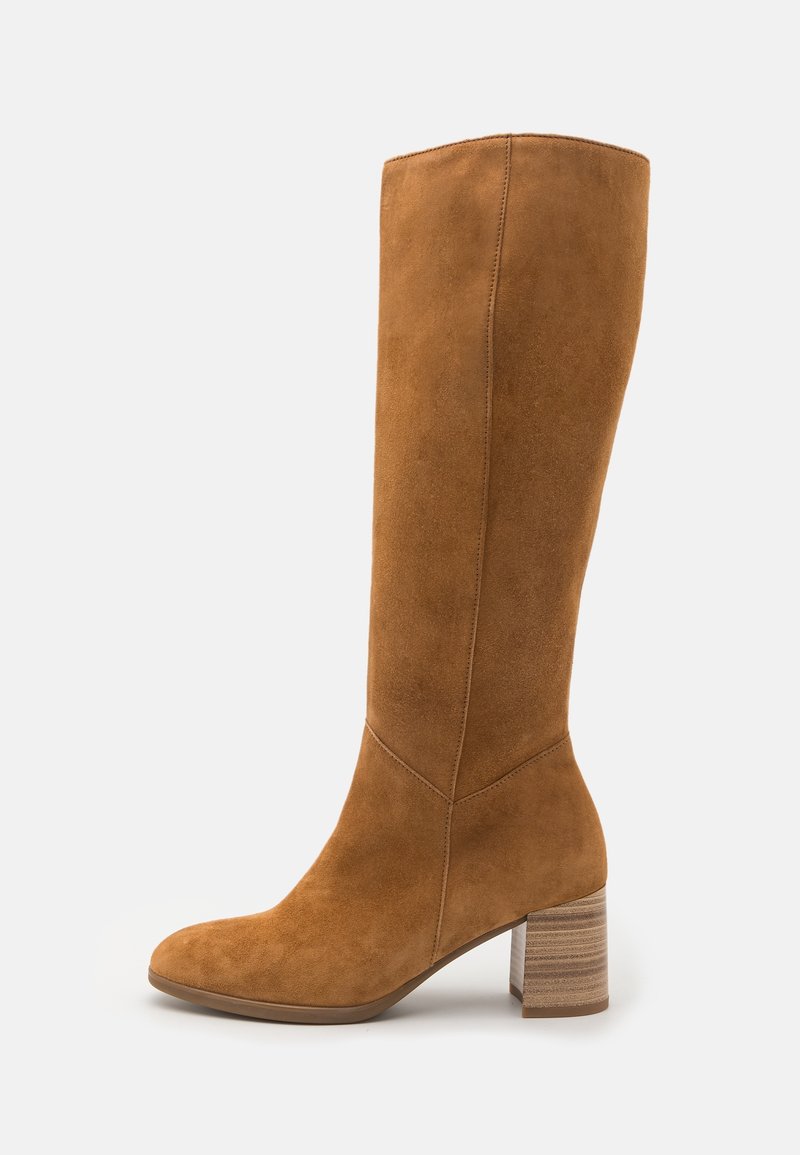 Botte haute jusqu'au genou en daim marron avec un bout arrondi, un talon empilé et des coutures décoratives sur les côtés. Texture lisse avec une finition douce.