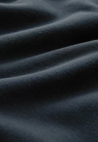 Tessuto scuro con una superficie morbida e texturizzata, che mostra pieghe delicati e una lucentezza liscia. Il colore è un nero profondo e ricco.