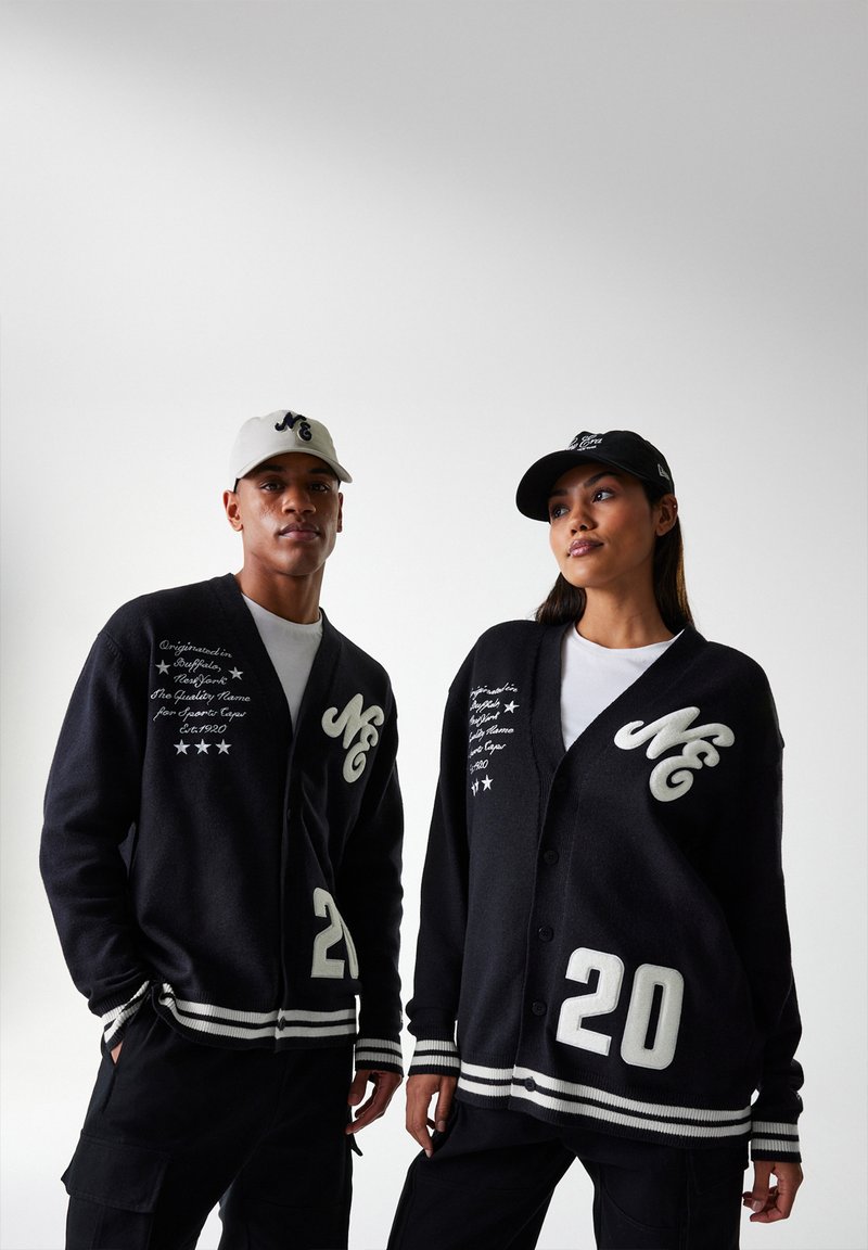 Cardigans en tricot noir avec des accents crème. Les caractéristiques comprennent des boutons surdimensionnés, des logos "MC" et des poignets rayés blancs. Tous deux portent des casquettes.