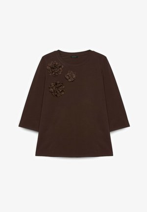 Bruine top met lange mouwen en drie donkerbruine stoffen bloemenapplicaties op het linker schoudergedeelte.