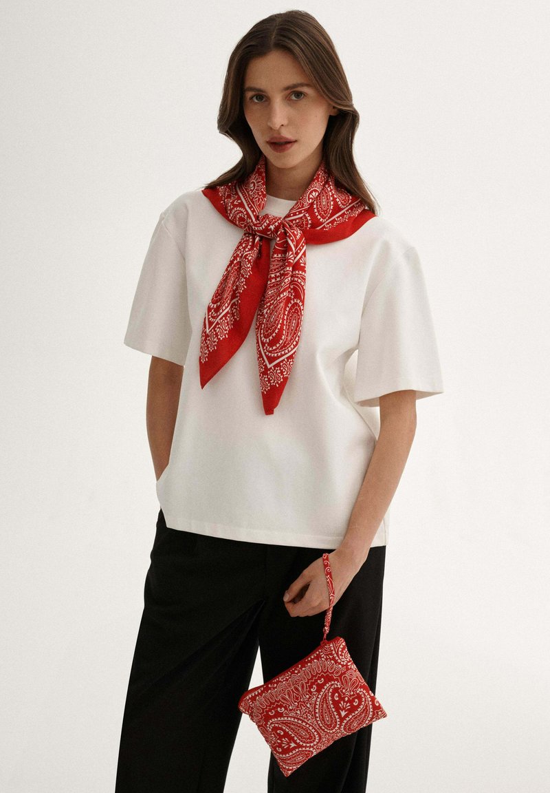 Biała koszula z krótkim rękawem w zestawieniu z czerwoną chustą w wzór paisley oraz pasującą małą torebką, charakteryzującą się teksturowanym materiałem i usztywnionym fasonem.