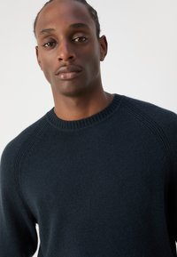 Maglione blu navy realizzato in morbido tessuto a maglia, con scollatura a girocollo, bordi a coste e maniche raglan con dettagli di cucitura sottile.