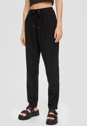 Pantalones joggers de lino negro con un corte relajado, cintura con cordón y textura sutil. Combinados con sandalias de plataforma negras y gruesas.