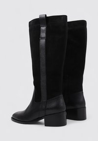 Botas negras hasta la rodilla que combinan ante y cuero texturizado, con un tacón cuadrado y un detalle decorativo en la correa trasera.