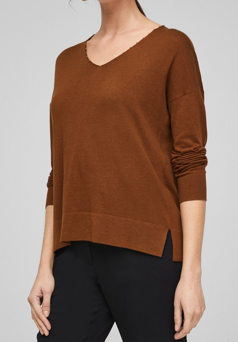 Brun V-hals tröja med rullade ärmar, sidslitsar vid fållen, och en mjuk textur. Tillverkad av ett lätt stickat tyg.
