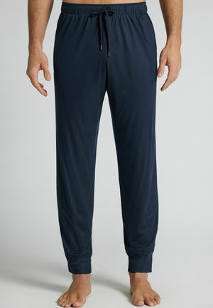 Man draagt marineblauwe joggingsbroek met elastische tailleband en trekkoord, staat op blote voeten op een lichtgrijze vloer.