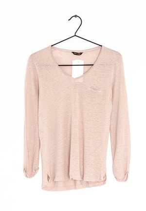 Jasnobeżowa, długorękawowa koszula z dekoltem w serek, małą kieszonką na piersi i bocznymi rozcięciami, zawieszona na czarnym wieszaku z białą metką.