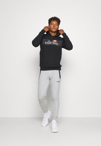 Schwarzer Hoodie mit Logo, graue Trainingshose und weiße Sneakers. Der Hoodie verfügt über eine Fronttasche und einen verstellbaren Kordelzug. Lässige Sportbekleidung.
