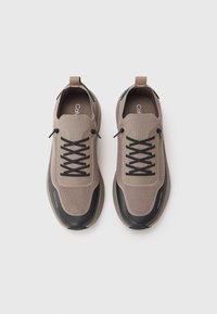 Beige mesh treningersko sko med sorte gummisåler, snøredesign og Calvin Klein-merke på siden og tungen.