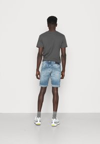 Mörkgrå T-shirt, ljusblå denimshorts med uppvikta fållar, grå strumpor och gråvita sneakers, sedd bakifrån.