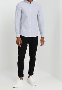 Ljusblå skjorta med långa ärmar och krage, i kombination med svarta byxor och vita sneakers. Enkelt och stilrent design.