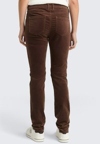 Bruine corduroy broek met een getailleerd ontwerp, vijf zakken, achterpand en contrasterende stiksels, gecombineerd met witte sneakers.