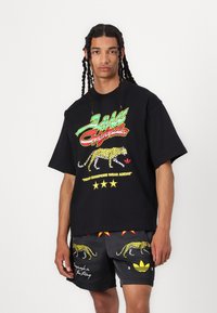 Black oversized t-shirt with colorful "Adidas Originals" graphic, featuring a leopard print and text details. Gray shorts with leopard accents.