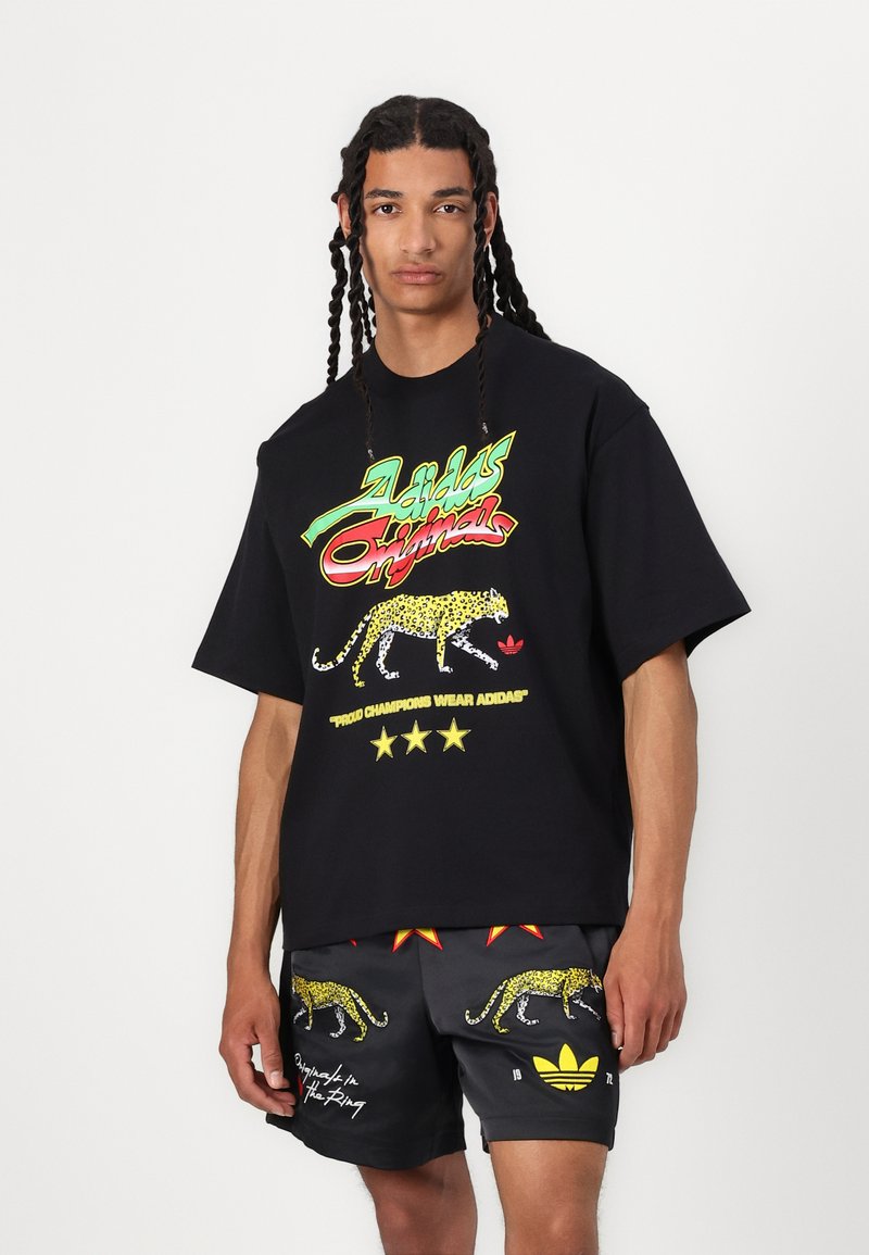 Black oversized t-shirt with colorful "Adidas Originals" graphic, featuring a leopard print and text details. Gray shorts with leopard accents.