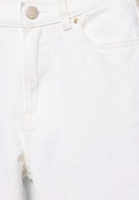 Sekcia bielych džínsových nohavíc zobrazujúca pás, gombík, predné vrecko a očká na opasok.