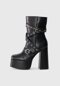 Zwarte high-heeled platformlaarzen van leer, voorzien van kruisbanden met zilveren hardware, studs en een vierkante neus.