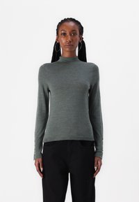 Grønn genser med lange ermer, høy hals og tettsittende design. Har knappdetaljer på ermene og et glatt, strukturert stoff.