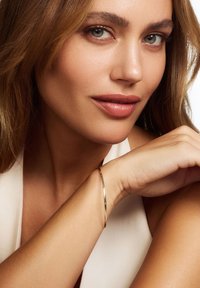 Gold bangle bracelet on an arm, featuring a sleek, smooth design with a polished finish, against a light neutral background.