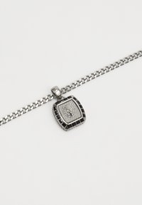 Collier en métal argenté avec un pendentif carré arborant un design de lion, entouré d'accents noirs et d'une surface texturée.
